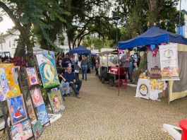 barracas de feiras com diversos produtos expostos; na esquerda, quadros