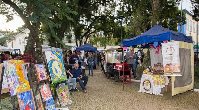 diversas barracas com produtos variados organizados em caminhos de pedras em praça arborizada