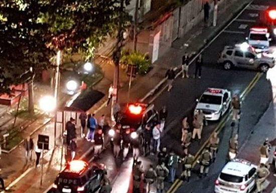 foto tirada do alto de um edifício mostra muitas viaturas paradas em volta de corpo no chão, com muitos policiais, ao lado de uma praça, onde populares olham