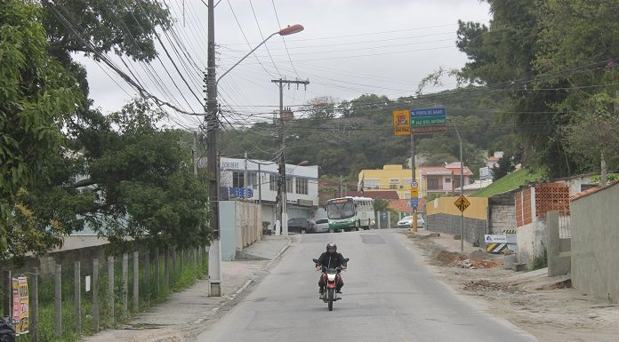 foto tirada no meio da rua onde há uma moto passando e obras no acostamento