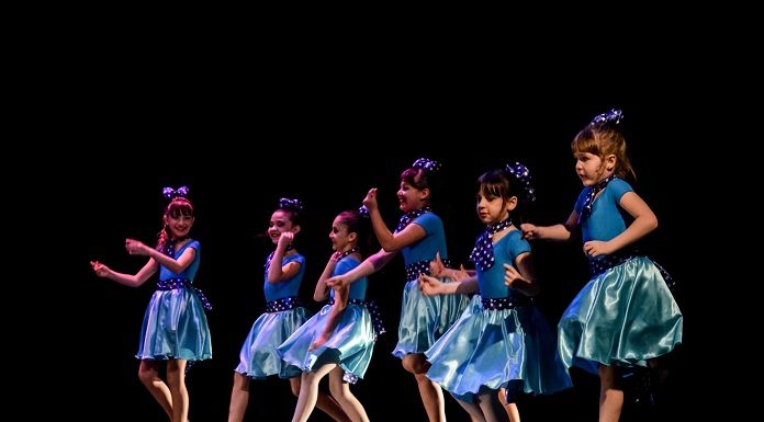 seis meninas com fantasias iguais dançam sorridentes lado a lado em um palco