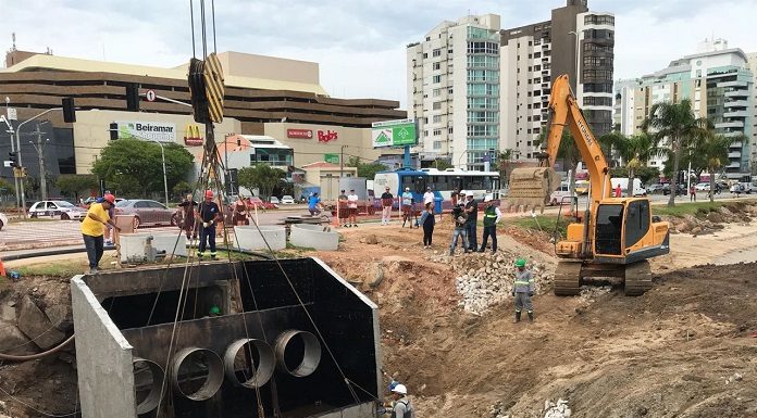 grande estrutura de concreto erguida por um guindaste sendo colocada em buraco no chão