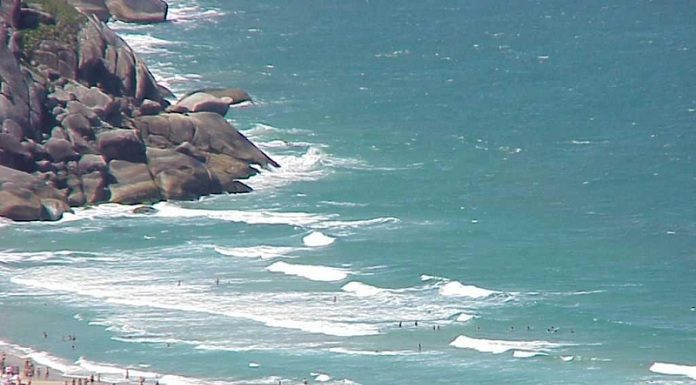 foto de uma praia em dia ensolarado com muitos banhistas vista de cima e de longe, como que de um prédio