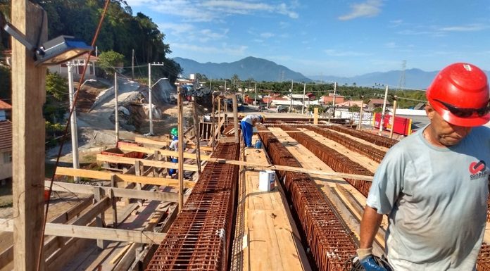 operário usando capacete anda sobre armação de ferro e madeira do elevado