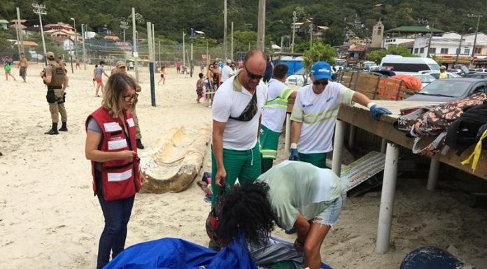 três pessoas conversam com morador de rua deitado em areia de praia