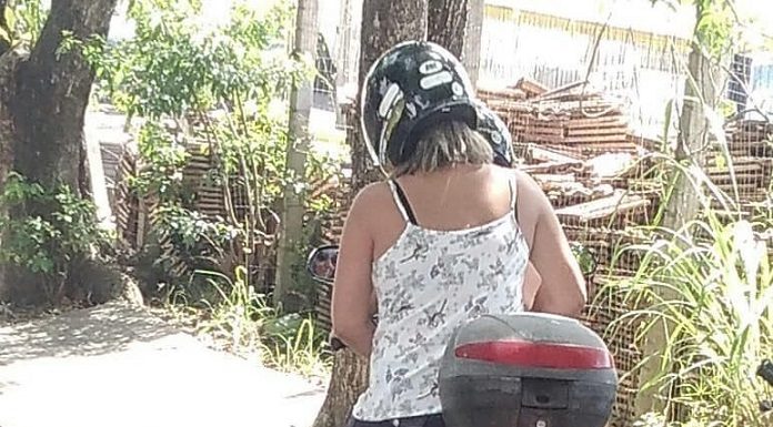 duas mulheres em uma moto paradas ao lado da calçada; placa e tatuagens estão censuradas