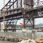 close na estrutura da ponte hercílio luz com uma bandeira de sc tremulando à frente