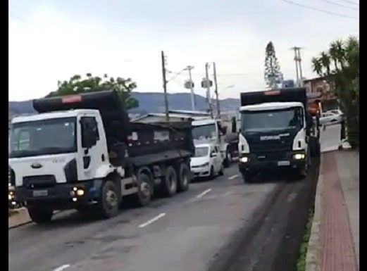 caminhões parados lado a lado na pistas da avenida com outros veículos atrás