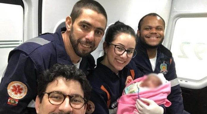 quatro profissinais do samu sorriem para selfie; a médica segura a neném no colo, que está com rosto borrado