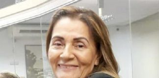 bernadete olha sorridente para a foto sentada em uma mesa