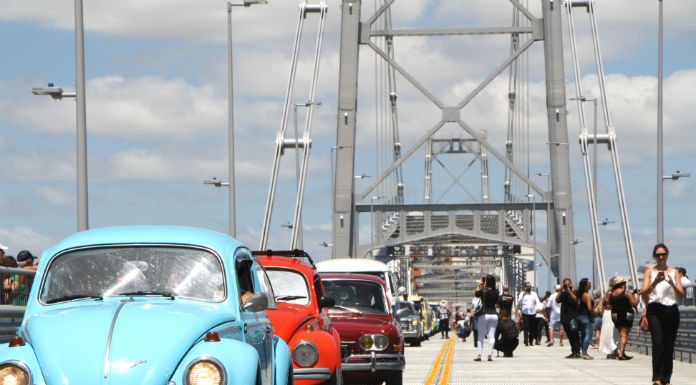 fuscas e outros carros antigos passando sobre a ponte Hercílio Luz com pessoas em volta