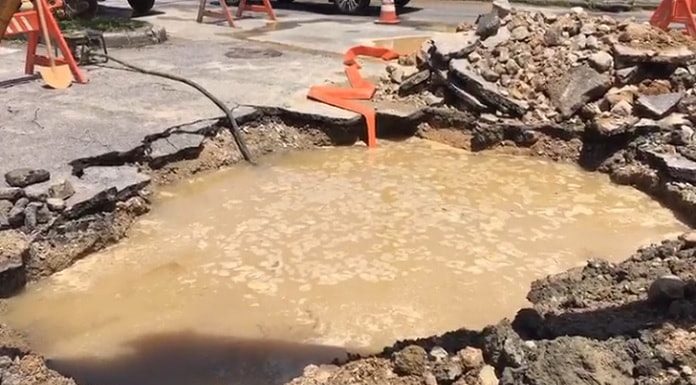 grande buraco com água na pista e entulhos em volta