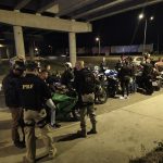 agentes da prf ao lado de diversas motos com pessoas em volta de noite