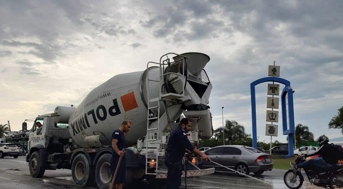 dois agentes da guarda limpam concreto caído atrás da betoneira e carros passando em volta