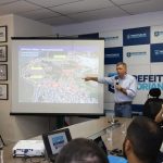 gean discursa em pé com microfone na mão apontando para uma imagem projetada de mapa da cidade