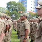 soldados da pmsc vistos de lado em pé alinhados em um gramado