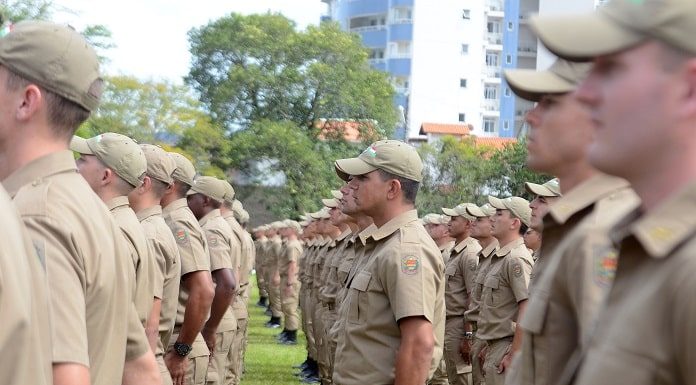 soldados da pmsc vistos de lado em pé alinhados em um gramado