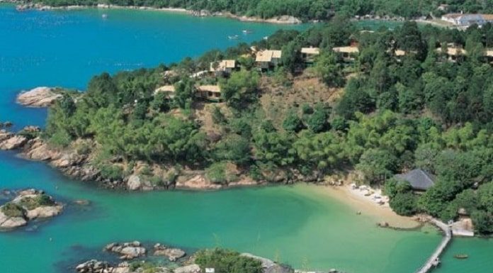 Resort de luxo : foto aérea do costão com o resort cheio de árvores e ilha à frente em mar esverdeado com ligação por ponte