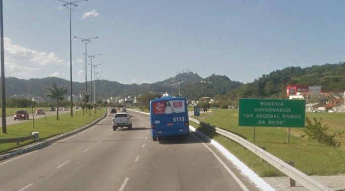 ônibus e carro passando pela via expressa sul e placa ao lado "rodovia aderbal ramos da silva"