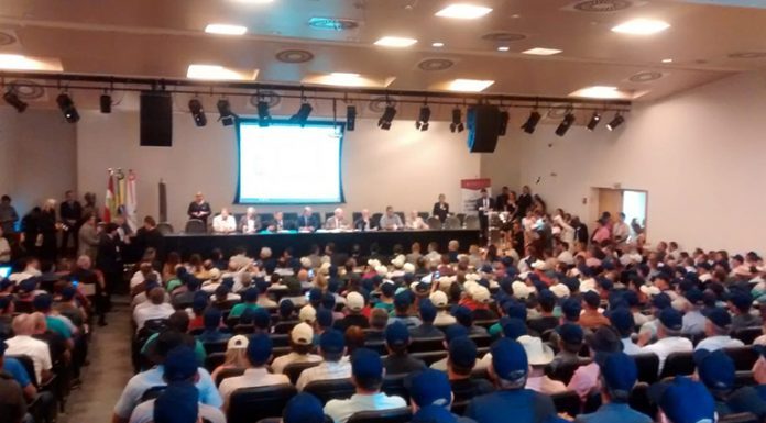 auditório lotado com maioria de homens de boné azul e outros brancos e no palco deputados em bancada