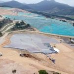 vista aérea do aterro sanitário de biguaçu, com boa parte de terra exposta, lonas por cima e máquinas circulando; montanhas ao fundo