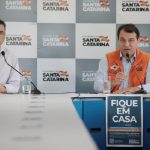 zeferino e moisés na ponta de uma mesa com cartaz à frente "fique em casa"