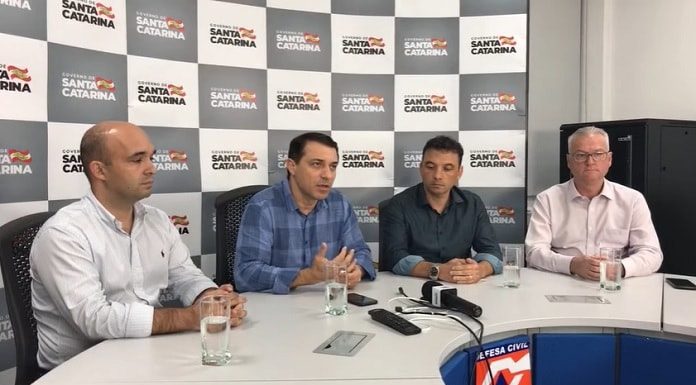 moisés em entrevista coletiva com mais três secretários e painel com logos do governo de sc ao fundo