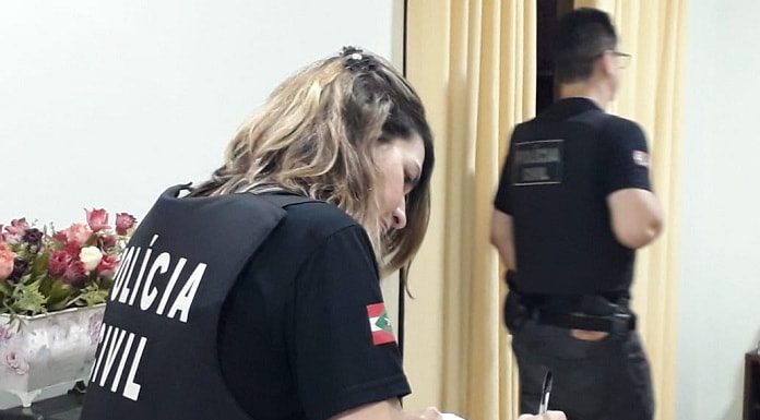 agente mulher da polícia civil com coleta à prova de balas com inscrição da pc escrevendo em prancheta sobre balcão