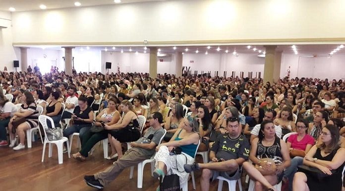 centenas de pessoas sentadas em cadeiras de plástico em grande salão