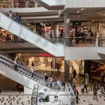 área central de um shopping com pessoas em escadas rolantes