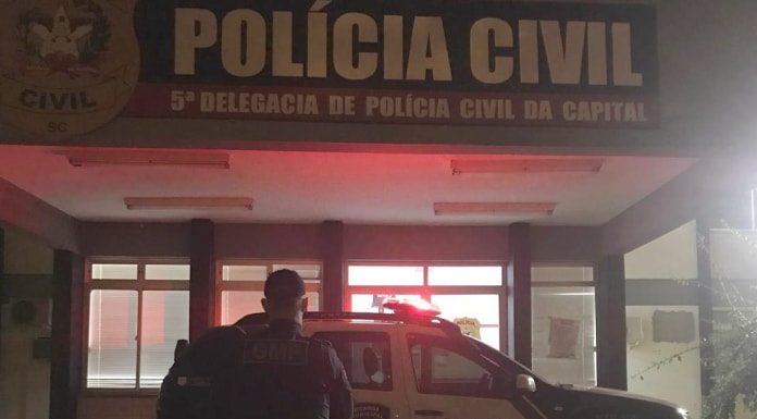 agente da guarda em frente à viatura estacionada em com luzes ligadas em frente à delegacia de polícia da trindade