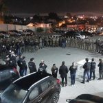 policiais civis e militares em pé em grande roda num estacionamento em foto noturna