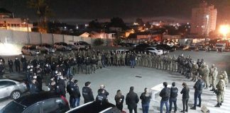 policiais civis e militares em pé em grande roda num estacionamento em foto noturna