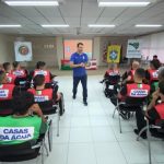 árbitro em pé dando aula em sala com outros homens usando colete da casas da água