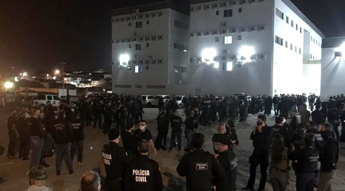 centenas de policias reunidos em pé em pequenos grupos em grande pátio com prédio ao fundo