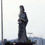 estátua de são josé usando máscara; é a estatua que fica na av. beira mar e mostra são josé segurando menino jesus; morro da cruz ao fundo