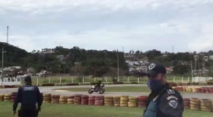 na pista do kartódromo agente faz sina de parada e outro anda em direção às barricadas de pneus; moto passando na curva