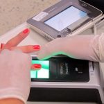 pessoa usando luvas tomas as digitais de mulher em aparelho de biometria