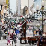 algumas mulheres de máscara andando no calçadão da felipe schimidt no centro de florianópolis; viatura ao fundo