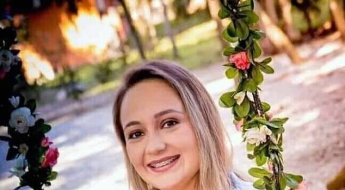 flavia godinho mafra em foto grávida sentada em balanço com flores segura um sapatinho de bebê sobre a barriga