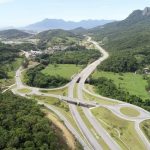 foto aérea do contorno viário onde há rotatórias e morro da pedra branca ao fundo