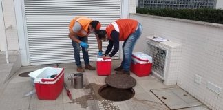 dois homens vestindo colete laranja, mexendo em uma caixa térmica vermelha