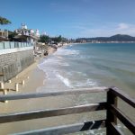 praia dos ingleses, com mar batendo nos muros da orla; guarda corpo de madeira em primeiro plano; praia ao longo até o fundo da foto