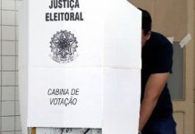 homem atrás de cabine de votação com o símbolo da justiça eleitoral