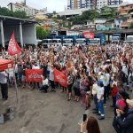 termina a greve da comcap com acordo de reajuste; centenas de pessoas reunidas em pátio da companhia; muitas com os braços para cima; tenda do sindicato à frente; caminhões ao fundo