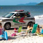 viatura suv da polícia passando por pessoas sentadas na areia da praia