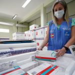 funcionária usando máscara e colete confere caixas de doses de vacinas dentro de caixas de isopor