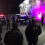 Policiais civis estão em circulo e uniformizados, no cenário ainda aparecem carros da polícia, eles cumpriram mandados e prenderam dois homens na operação de combate à pornografia infantojuvenil em Florianópolis