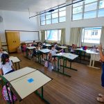 professora usando máscara dá aula para crianças em carteiras usando máscaras - doses para vacinação de professores